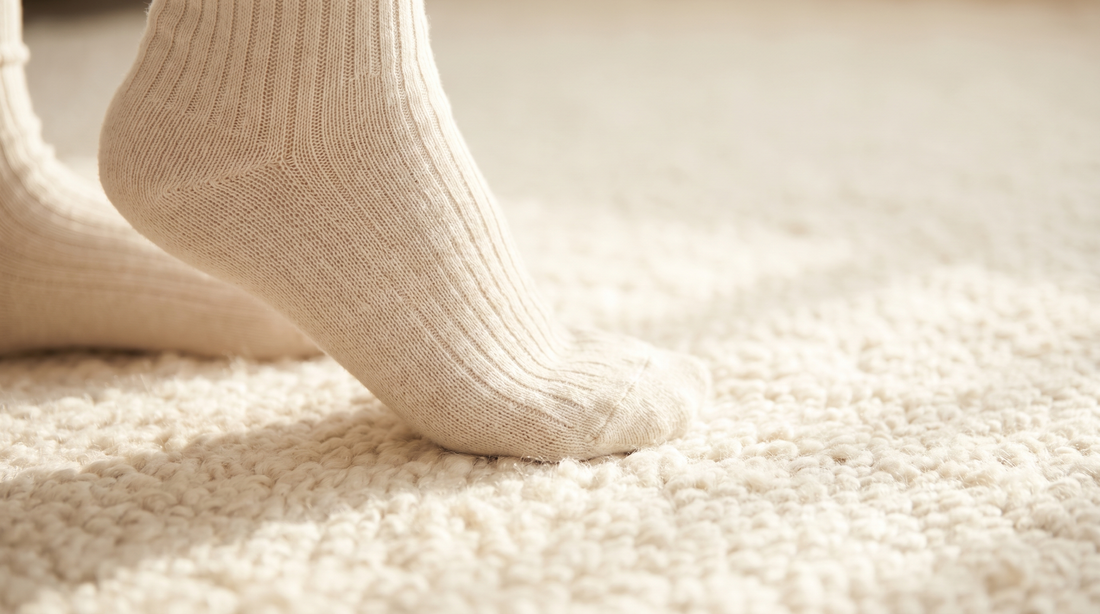 A foot in a soft sock pressing gently into a textured rug — editorial photograph on the sole's sensory role in posture.